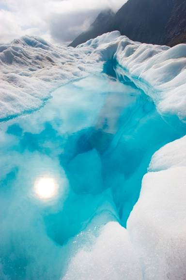 Bright blue glacial lake surrounded by white ice on a dark mountain